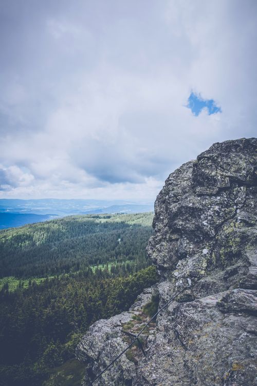 Free A scenic view from a rocky cliff overlooking a dense forest under a cloudy sky. Stock Photo