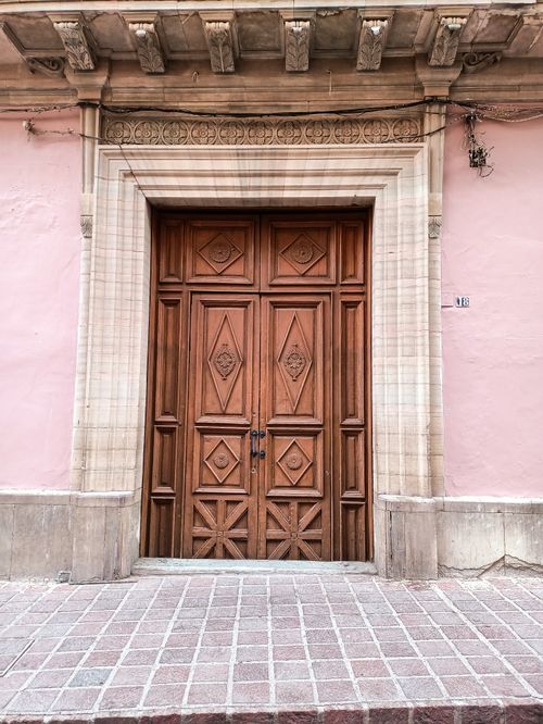 Free Classic wooden door with intricate carvings set in a pink walled exterior, exuding vintage charm. Stock Photo
