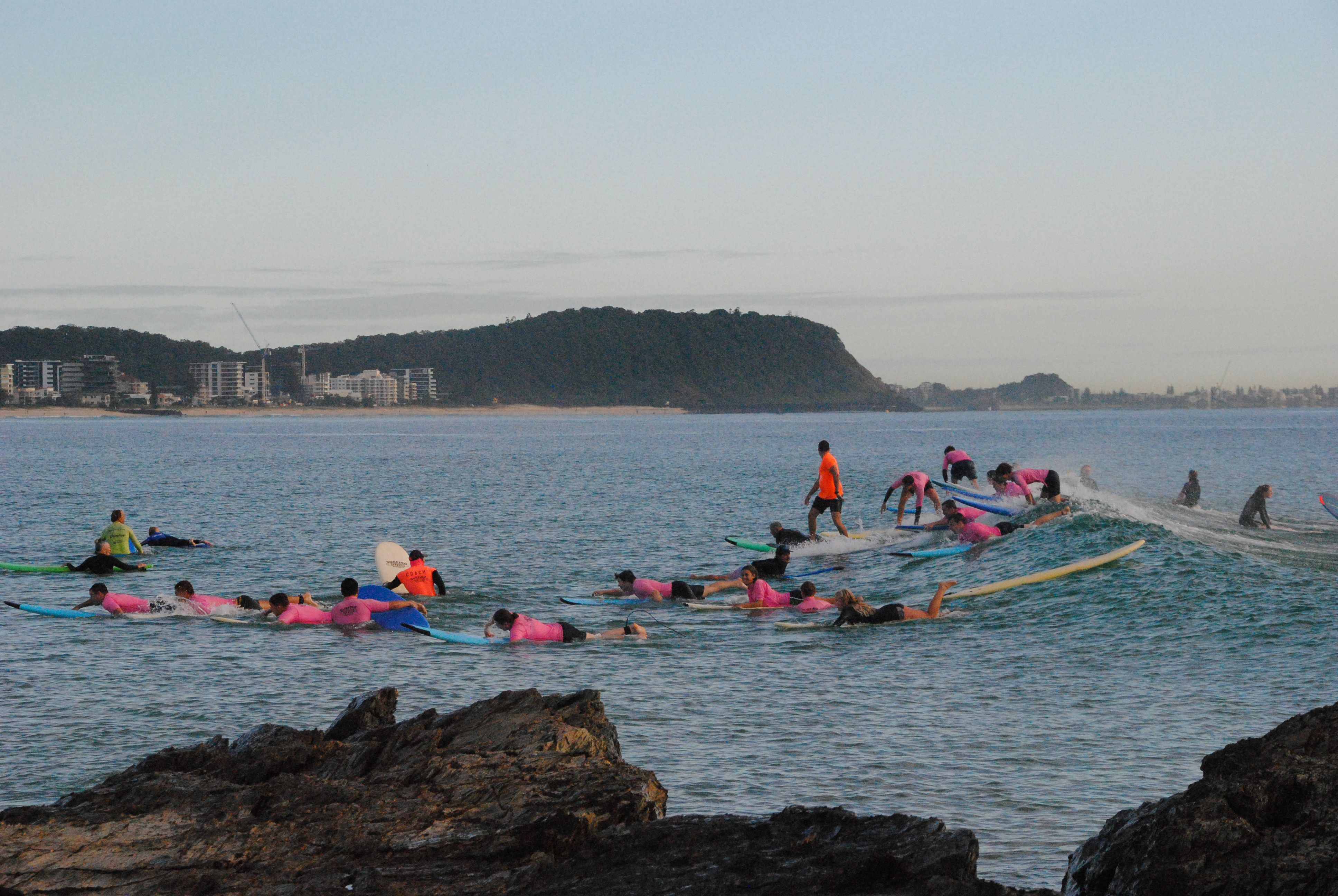 Surfing group lesson near scenic coastline, vibrant attire, dynamic formations.