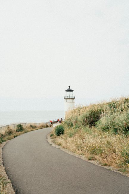 A picturesque lighthouse standing by a winding coastal pathway, under an overcast sky.