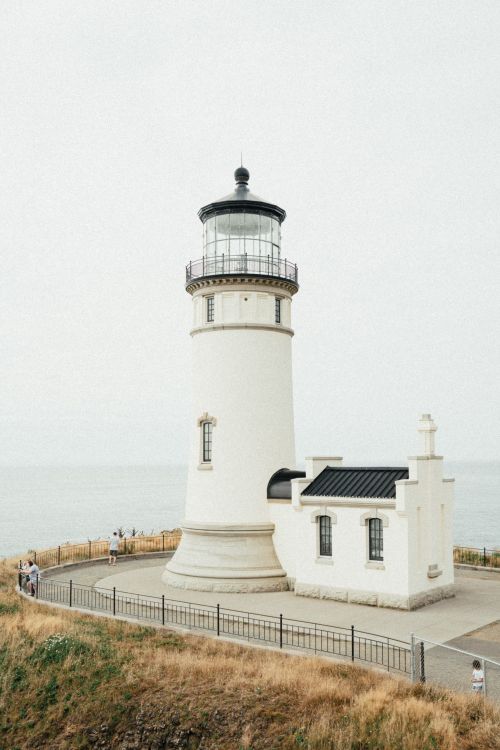 Free A solitary white lighthouse stands by the sea surrounded by grass under a summer sky. Stock Photo