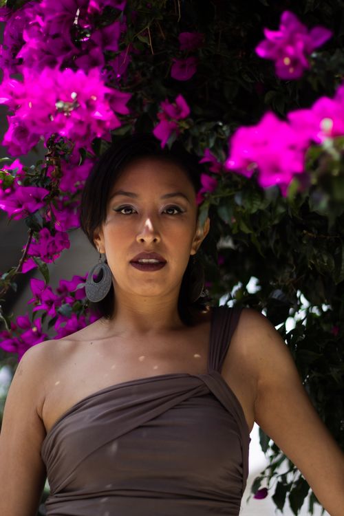 Free Elegant portrait of a woman with bold earrings framed by vivid pink bougainvillea blossoms outdoors. Stock Photo