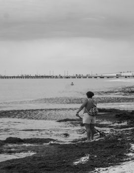 A woman stands on a tranquil beach, gazing at the ocean. Captured in classic black and white.