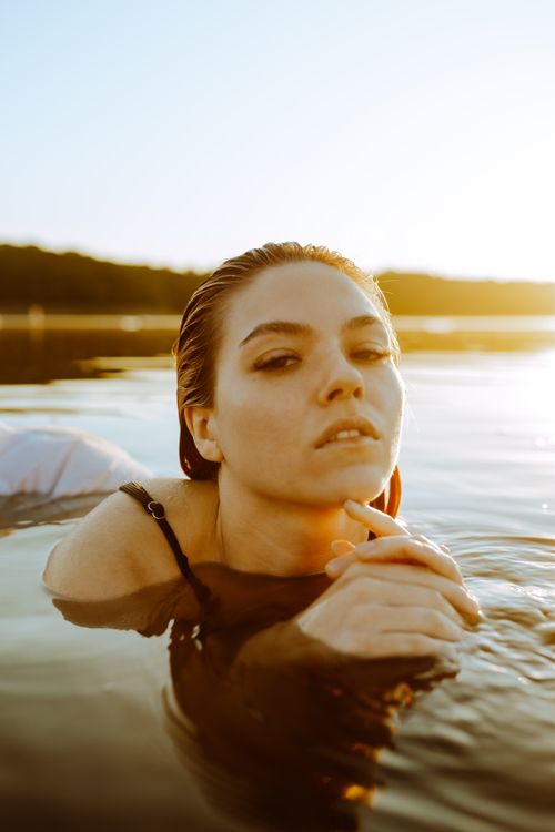 Free A woman with wet hair enjoys a tranquil moment in a lake at sunset, reflecting serenity and beauty. Stock Photo
