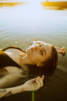 A woman lies peacefully in water during sunset, creating a serene and tranquil scene.