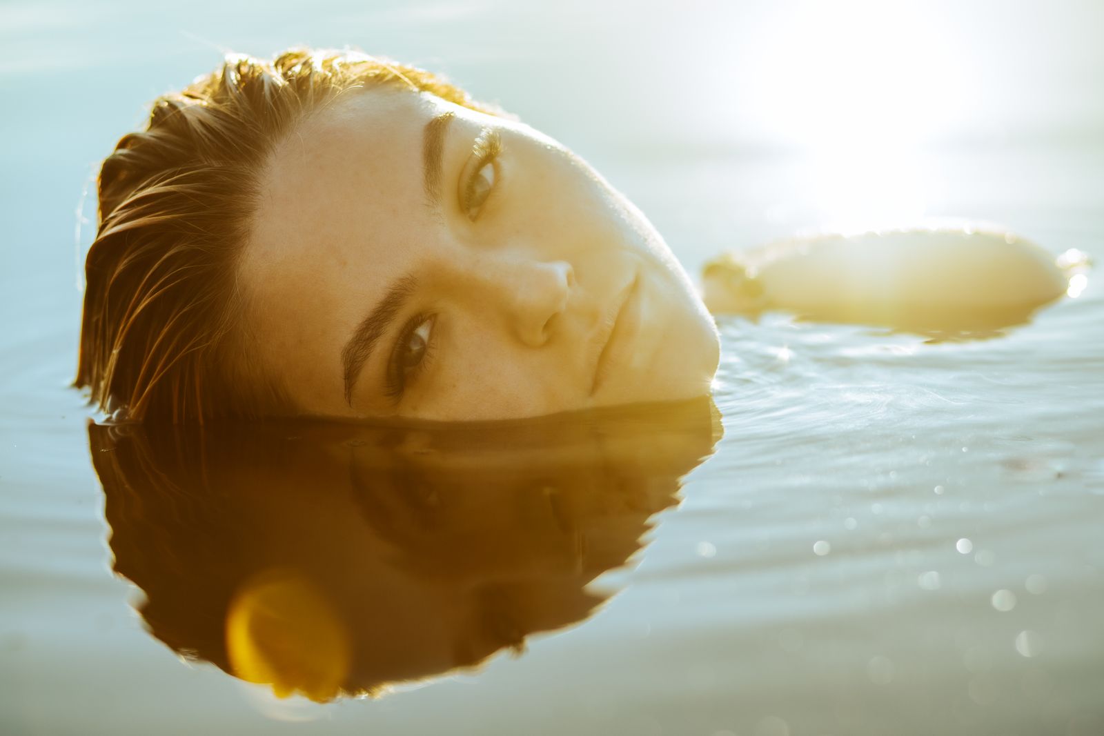 A serene portrait of a woman relaxing in the calm water with sunlit reflections creating a peaceful ambiance.