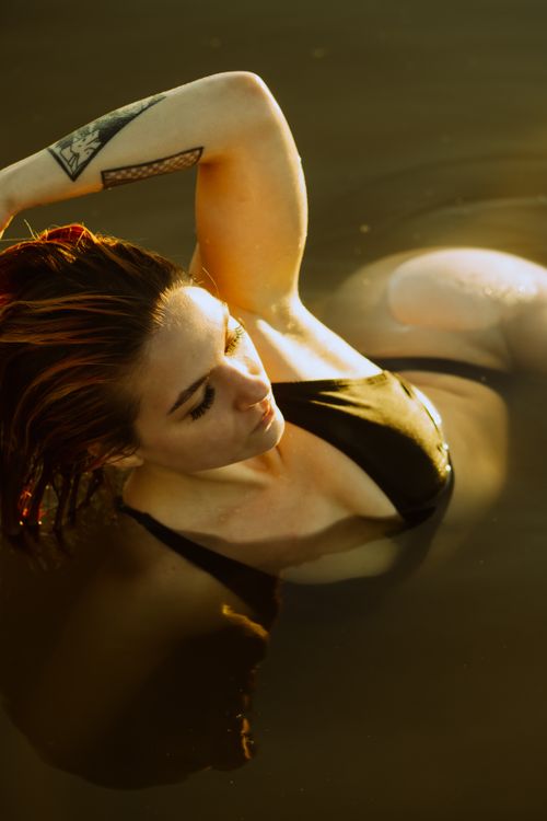 Free A woman with tattoos relaxes in water, showcasing serene beauty and conceptual art. Stock Photo