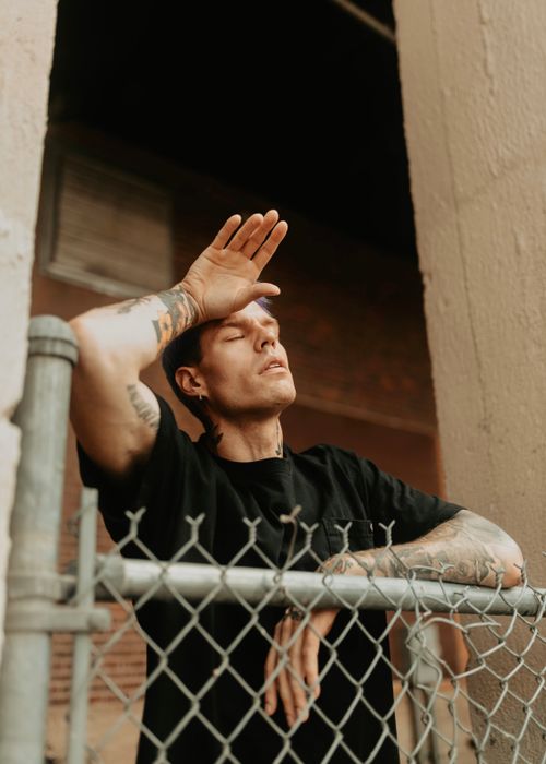 Free Tattooed man with dyed hair poses outdoors in Des Moines, IA, leaning on a chain-link fence. Stock Photo