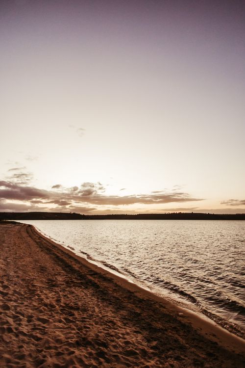 Free A peaceful beach scene at sunset, showcasing golden sand and calm waters under a clear sky. Stock Photo