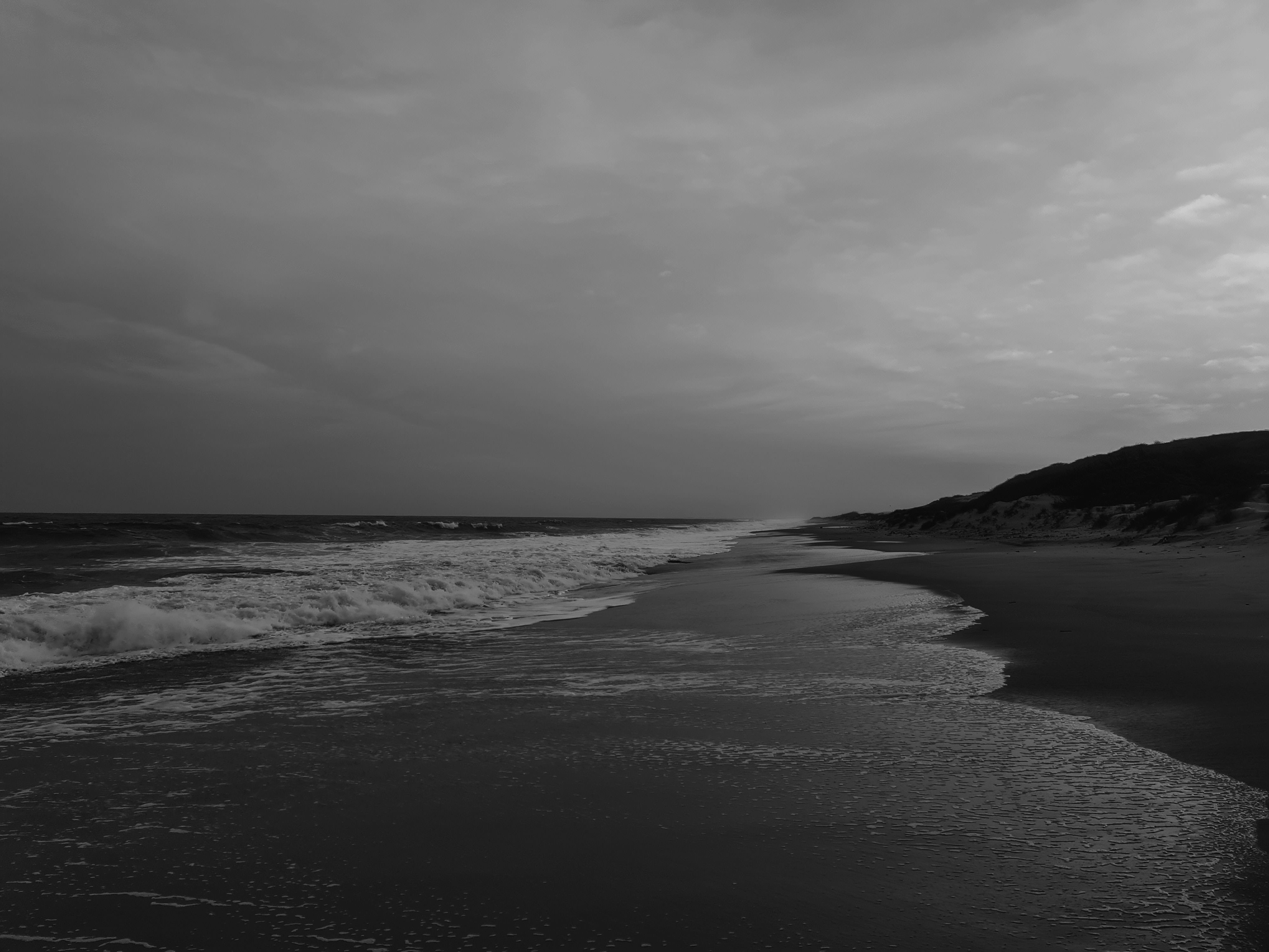 Serene monochrome beach with gentle waves and cloudy sky.