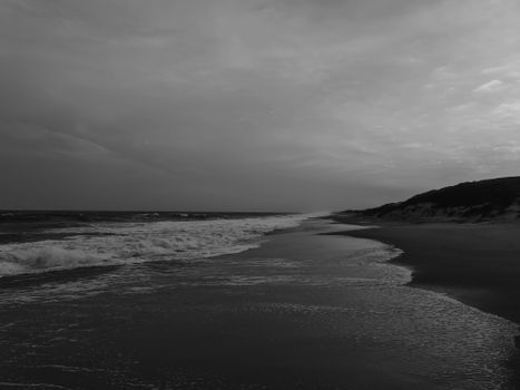 Serene monochrome beach with gentle waves and cloudy sky.
