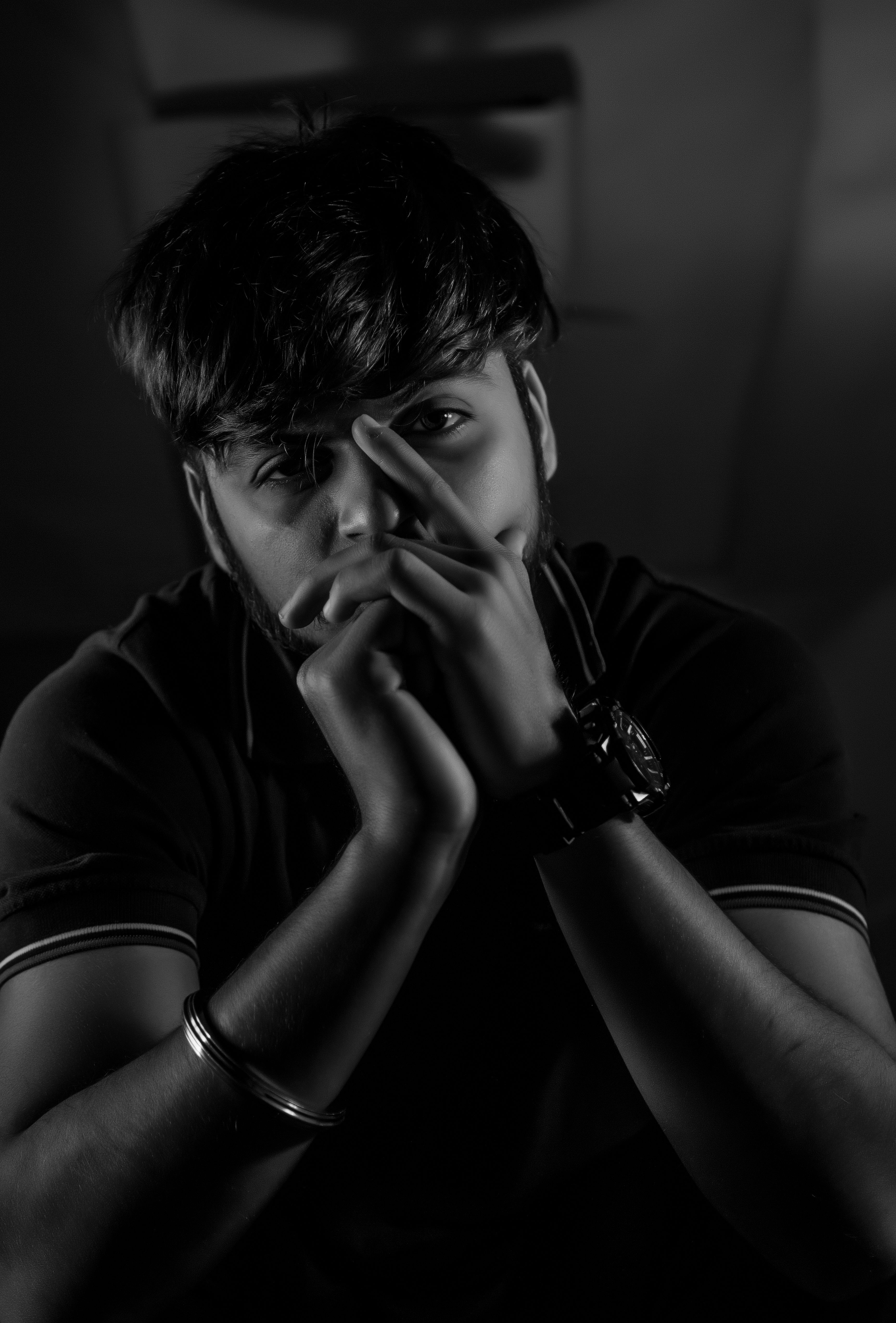 A thoughtful young man in a black and white portrait, hands on face in a dark mood.