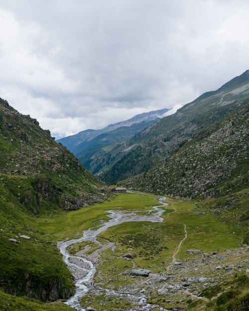 Free A breathtaking aerial view of a lush, scenic mountain valley with a winding river under a cloudy sky. Stock Photo