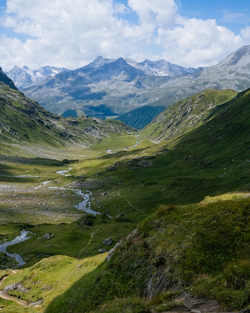Free Scenic mountain valley with lush greenery and winding stream under a bright sky. Stock Photo