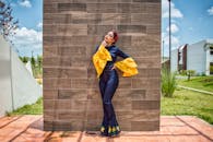 一位穿着五颜六色服装的年轻女子在户外的纹理墙前摆姿势，明亮又时尚