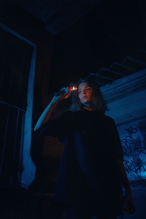 Free Artistic portrait of a woman holding a lit matchstick in a dark urban environment. Stock Photo