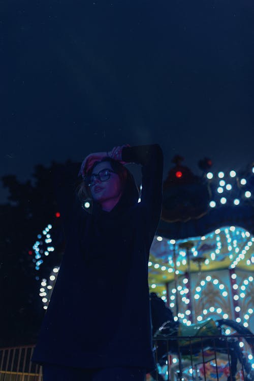 A Woman in Black Cardigan Standing Near a Carousel During Night Time
