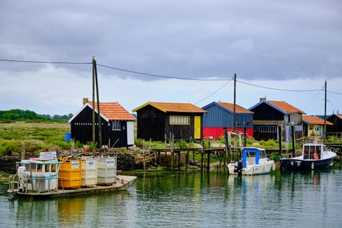 Free Scenic view of vibrant wooden houses along a riverside with boats and grassy fields under a cloudy sky. Stock Photo