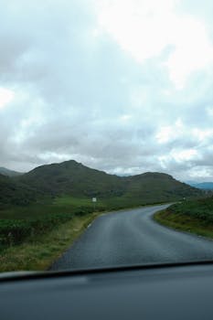 A tranquil winding road through lush green hills under a cloudy sky, perfect for nature lovers.