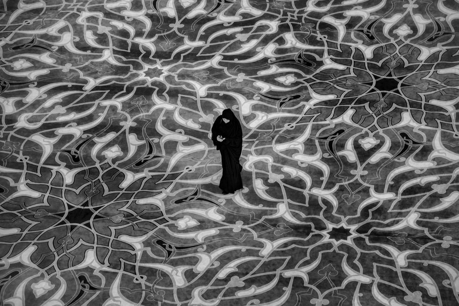 A woman in traditional attire stands on an intricate mosaic design seen from above.