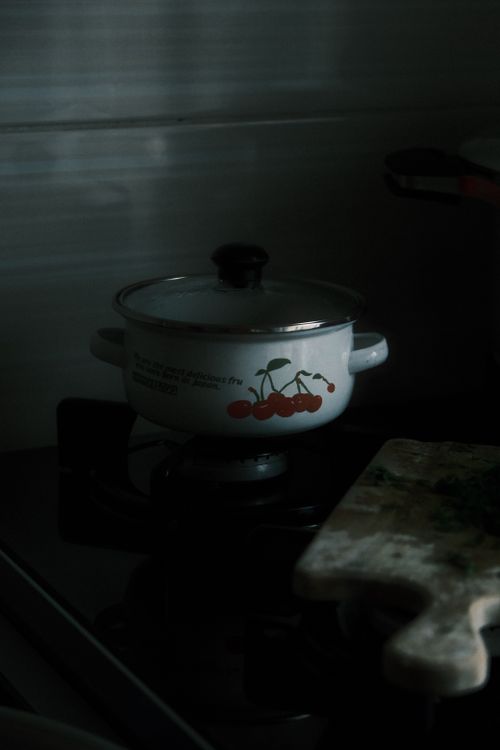 Free A vintage pot with cherry design on a gas stove in dim lighting. Cozy kitchen atmosphere. Stock Photo