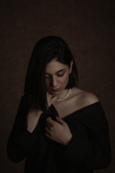 Portrait of a woman posing elegantly against a dark background wearing a black dress.