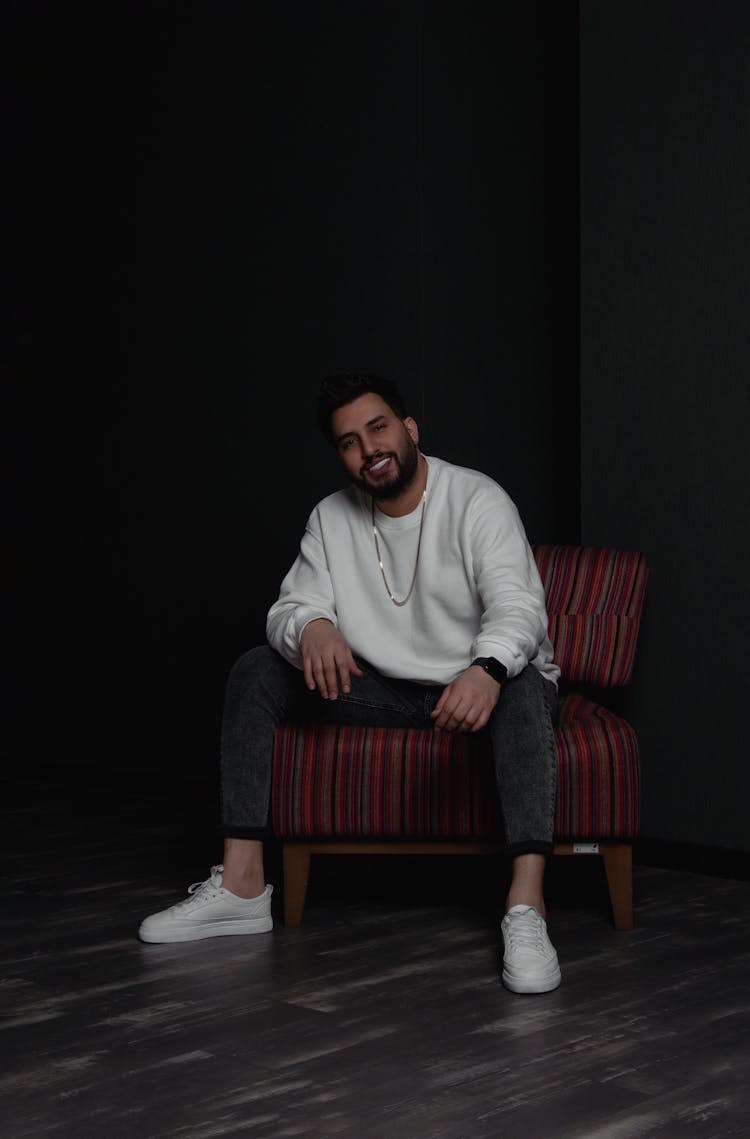 Man In White Sweater Smiling And Sitting On A Single Sofa 