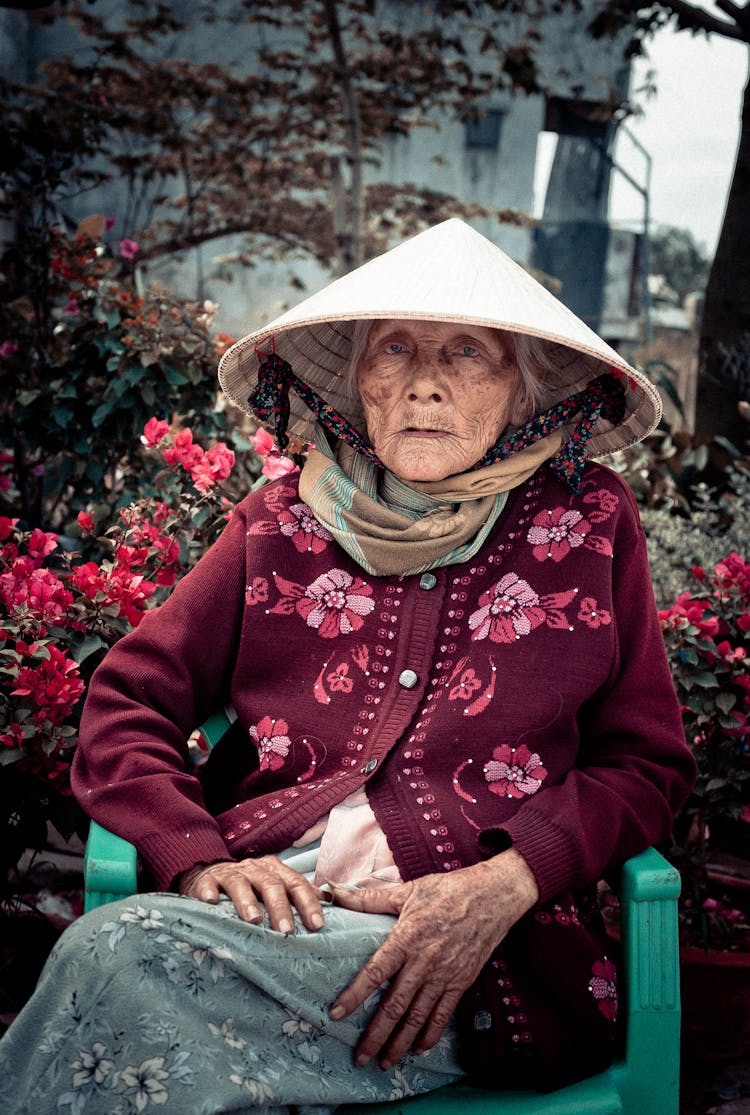 Old Woman In Traditional Conical Hat Sitting In Chair