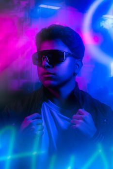 Teenage boy in sunglasses striking a pose against a vibrant neon light backdrop.