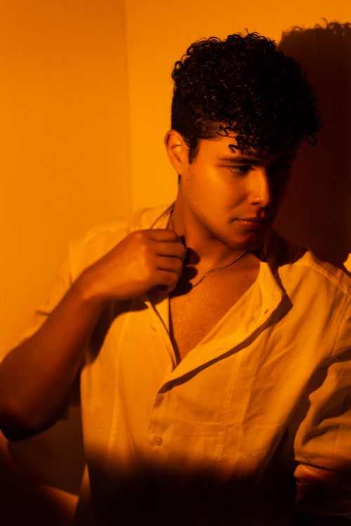 Free Portrait of a man in a white shirt with curly hair, bathed in warm yellow lighting. Stock Photo