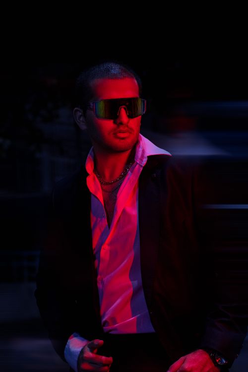 Free A fashionable man in a black blazer and sunglasses poses confidently under vibrant red lighting. Stock Photo