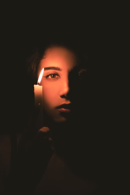 Free A woman holding a candle in darkness, casting a soft, mysterious glow. Stock Photo