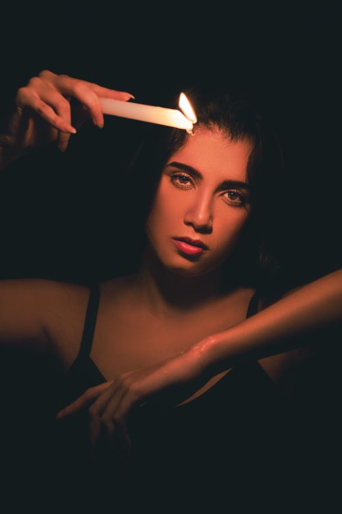Free Moody studio portrait of a woman holding a lit candle against a dark background. Stock Photo