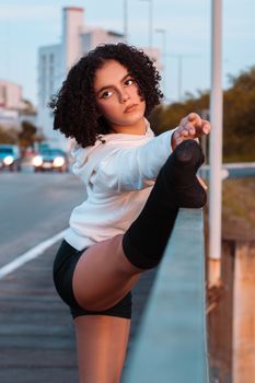 A young woman in a hoodie performs a stretch outdoors, showcasing fitness and flexibility.