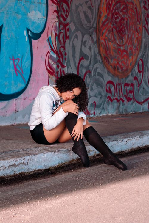Free Contemporary ballet dancer in casual attire poses in front of colorful graffiti, exuding modern artistic expression. Stock Photo