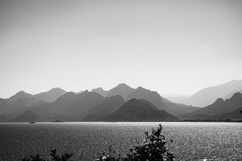 Free Monochrome photo of serene mountains and sea with sparkling water and clear sky. Stock Photo