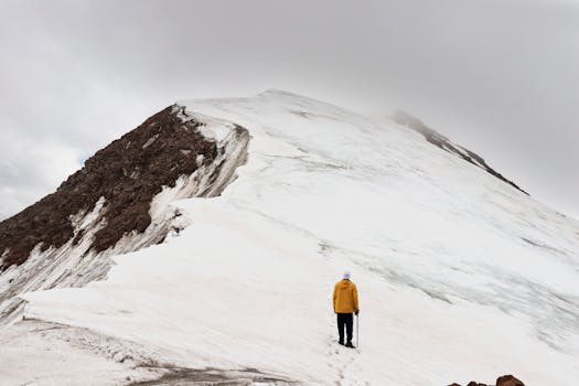一名登山者身着冬季装备，在多云的天空下登上了雪山
