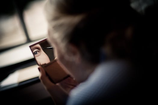 A woman intently applying eyeliner, captured in a reflective mirror close-up indoors.