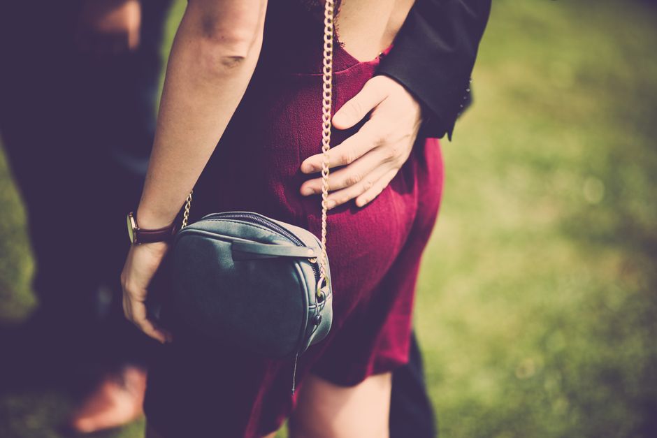 Fotomural Una mujer elegante con un vestido rojo y un bolso disfruta de un momento romántico al aire libre.