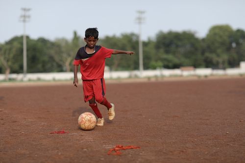 Free A young boy skillfully dribbles a soccer ball on a dirt field, enjoying a game outdoors. Stock Photo