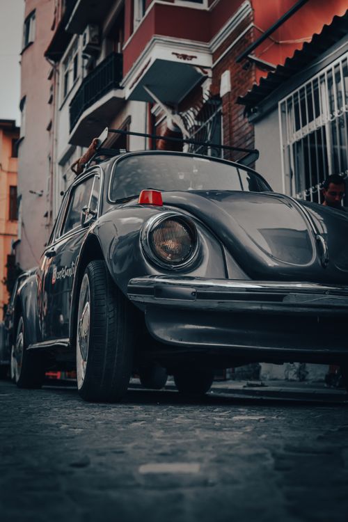 Free Classic Volkswagen Beetle parked on a cobblestone street, showcasing urban architecture. Stock Photo