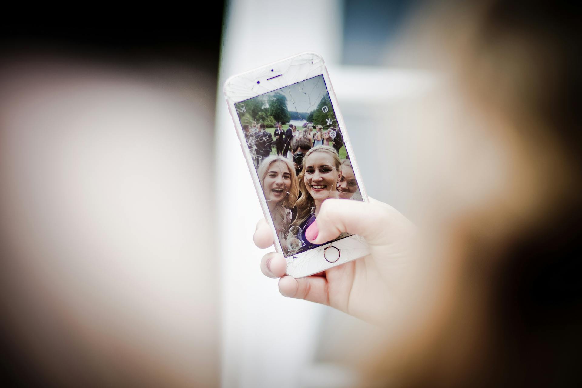 A group of women take a selfie outdoors with a smartphone featuring a cracked screen. Smiles and camaraderie captured in the moment.