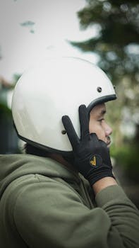 Side view of a man wearing gloves and adjusting his helmet outdoors.