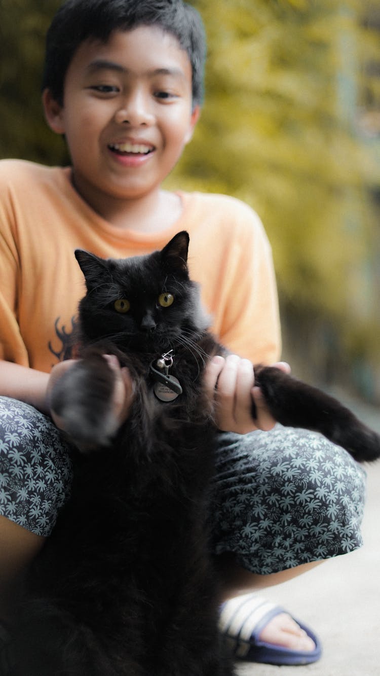 Smiling Boy Sitting And Holding A Black Cat