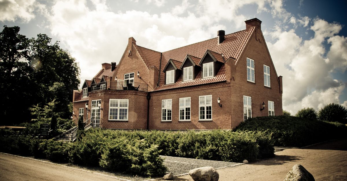Elegant brick mansion with landscaped garden under a bright sunny sky.
