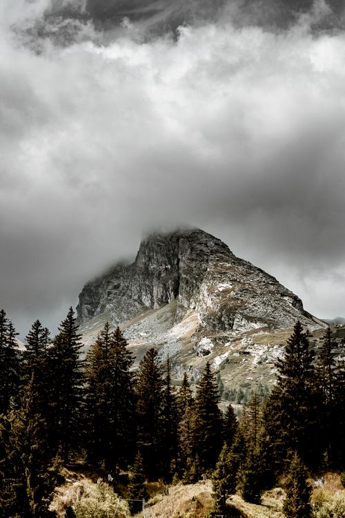 Free Majestic mountain peak enveloped in dark clouds, surrounded by a forest. Stock Photo