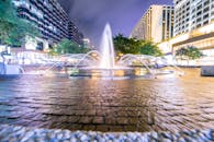 城市喷泉在夜间灯光下被照亮，与周围的现代建筑和充满活力的路灯相映成趣