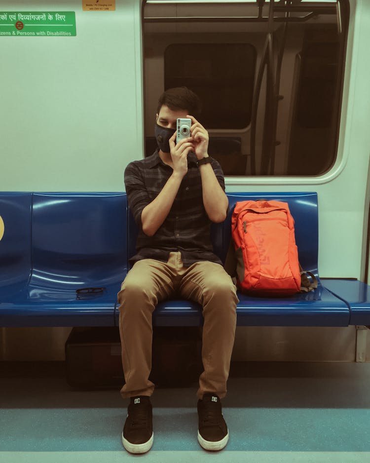 Man In Black Polo Shirt And Brown Pants Sitting On Blue  Seat On A Train