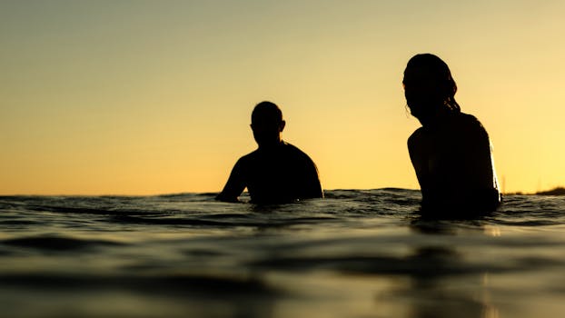 Silhouetted people enjoying the ocean at sunset, creating a serene, warm seascape.