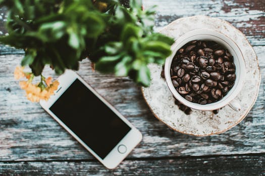 俯视智能手机旁装满咖啡豆的瓷杯和木桌上的鲜花